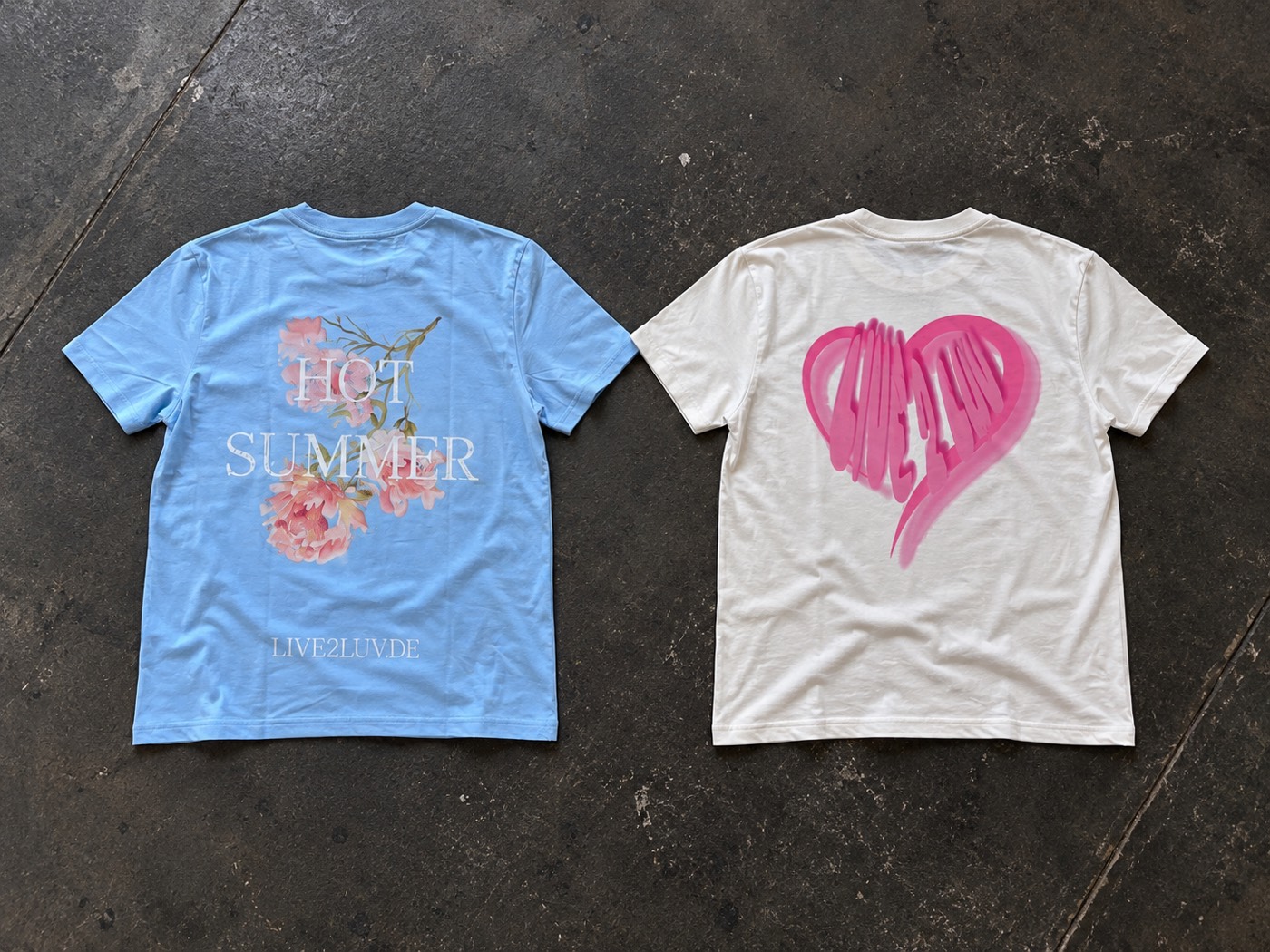 Zwei bedruckte Shirts von live2luv auf dem Werkstattboden: hellblau mit Blumenmotiv, weiß mit pinkem Herz